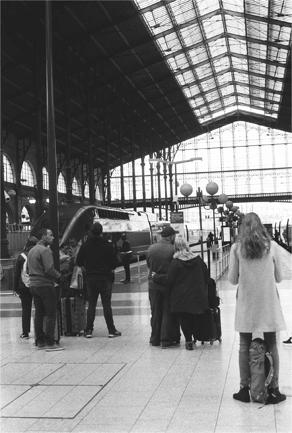 Fotografía en blanco y negro del interior de una estación ferroviaria con personas agrupadas junto a un tren detenido.