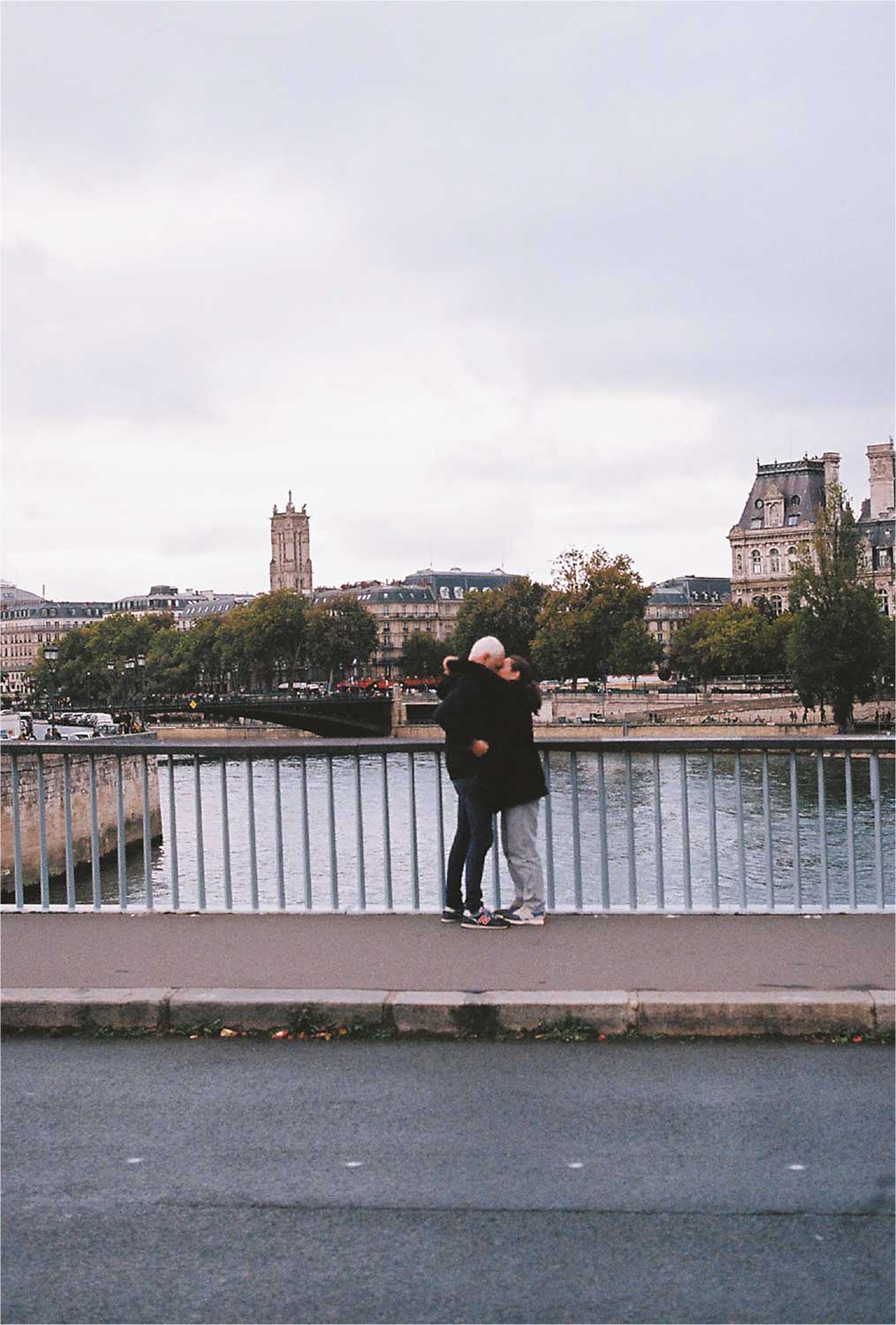 Fotografía de dos personas abrazadas sobre un puente urbano, con un río y edificios históricos al fondo.