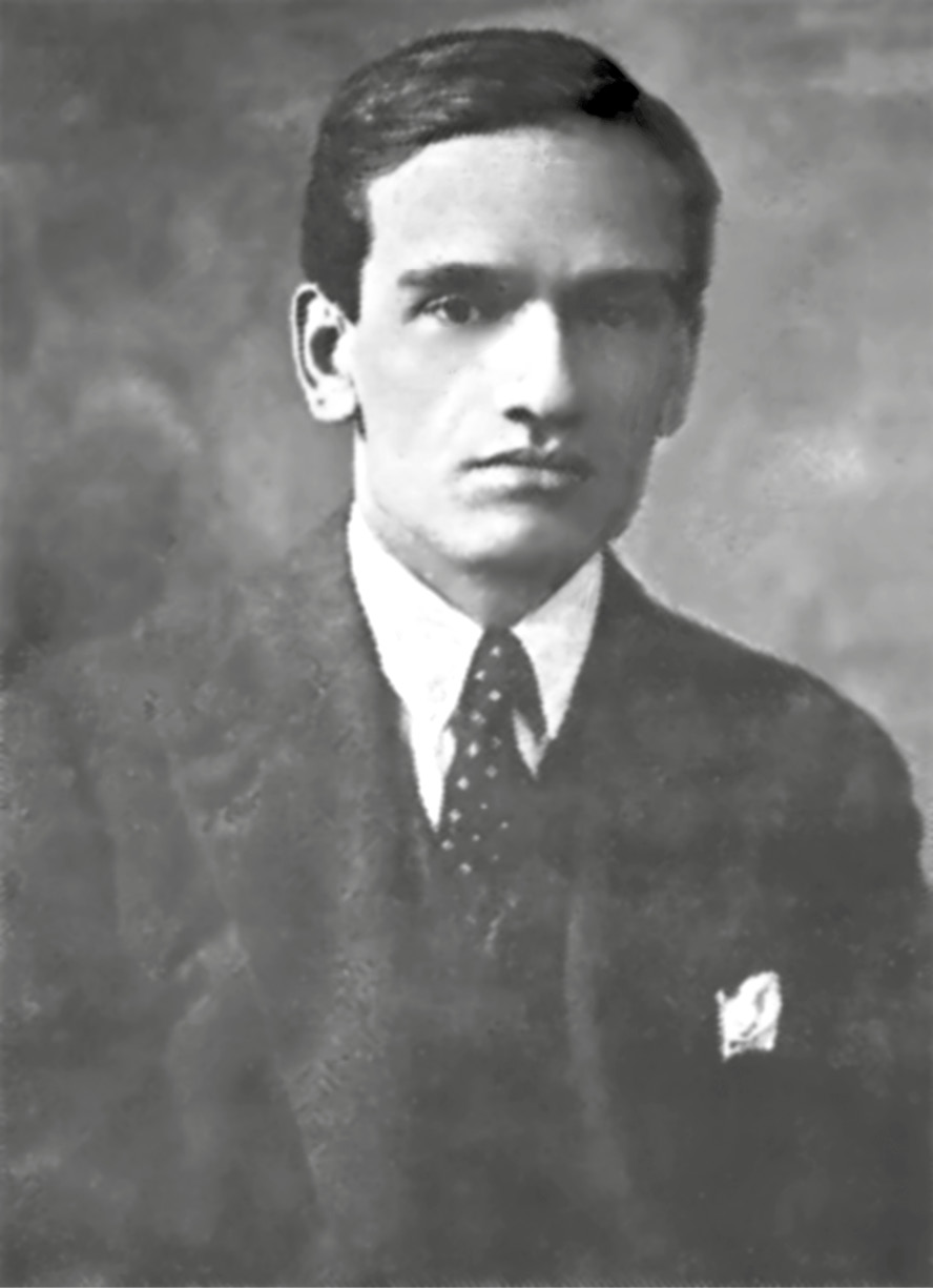 Fotografía estilo retrato de estudio en blanco y negro de César Vallejo, posando a cámara. Viste un traje oscuro, camisa blanca y corbata oscura con pequeños topos blancos dispersos, con un pañuelo blanco sobresaliendo del bolsillo de su americana a la altura del pecho.