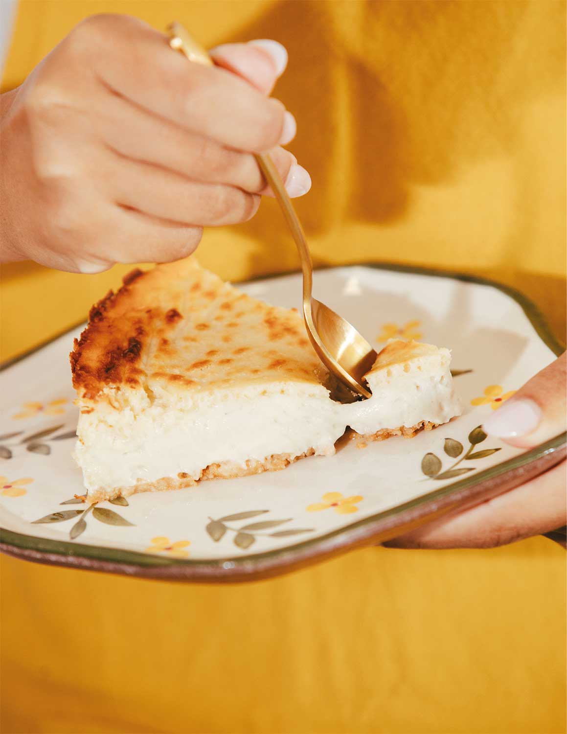 Fotografía en la que aparecen las manos de una persona sujetando una cuchara y un plato de cheesecake.